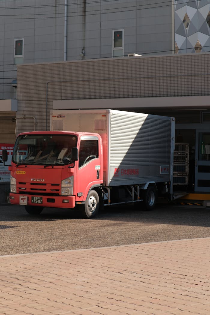 About A red delivery truck unloading goods at a warehouse on a sunny day in the city.