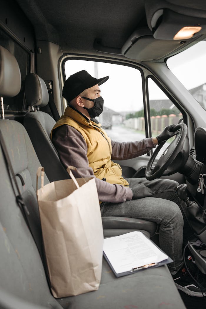About A masked delivery driver seated in a van, highlighting modern delivery services.
