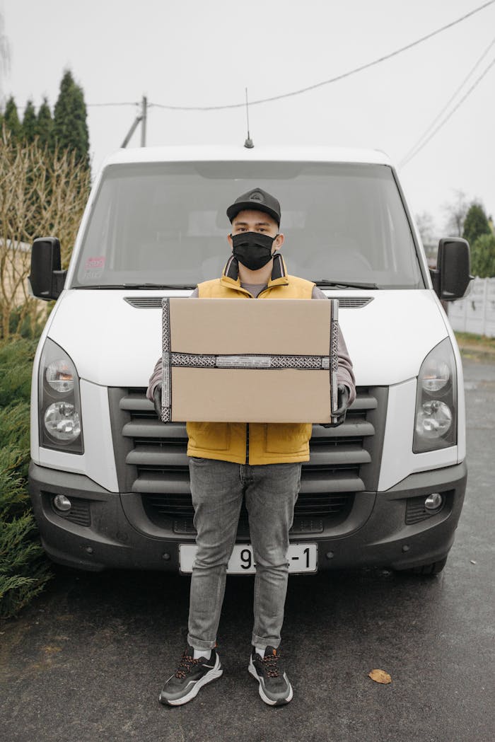 Delivery man with mask carrying package in front of a delivery van during the pandemic.
